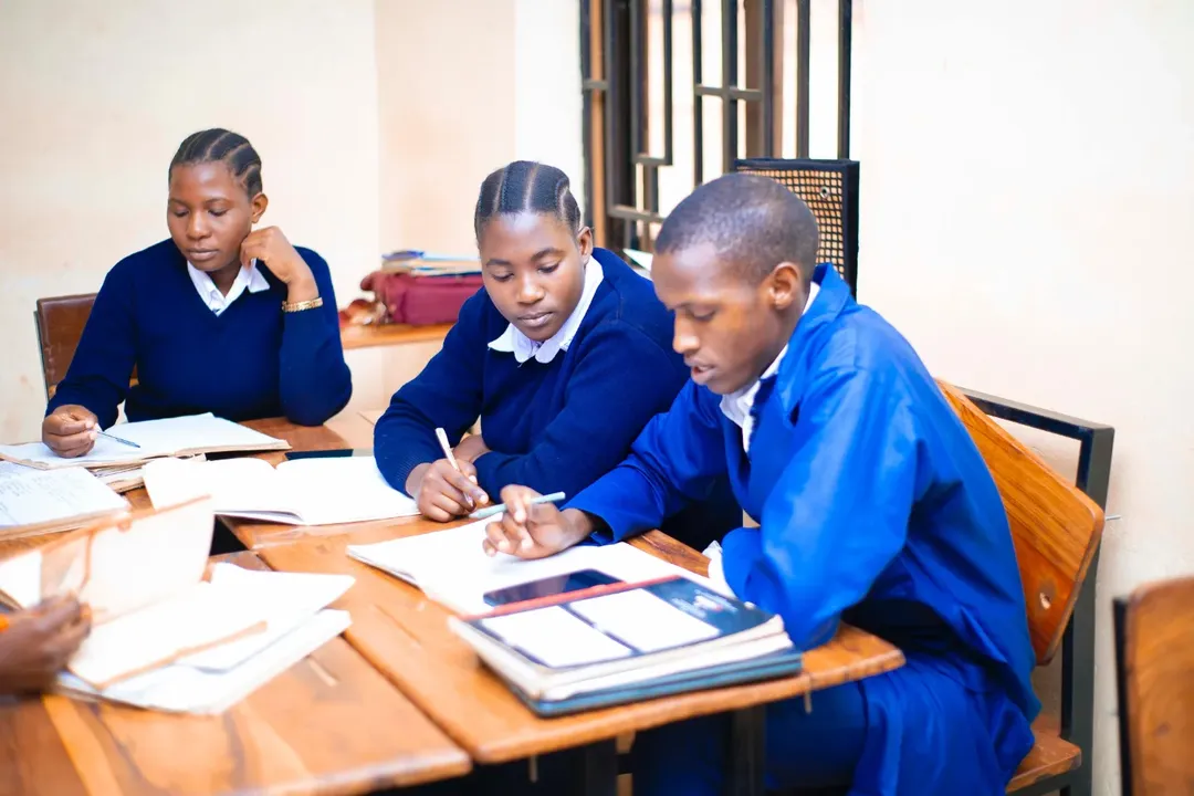 Three EHM students taking notes together at a shared study table inside a Folk Development College classroom