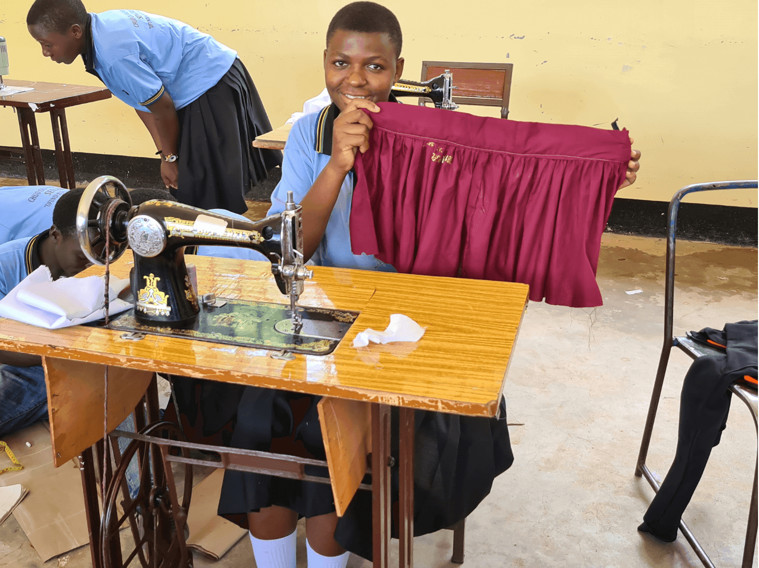 A tailoring student smiling with pride as she holds up the skirt she has just finished sewing
