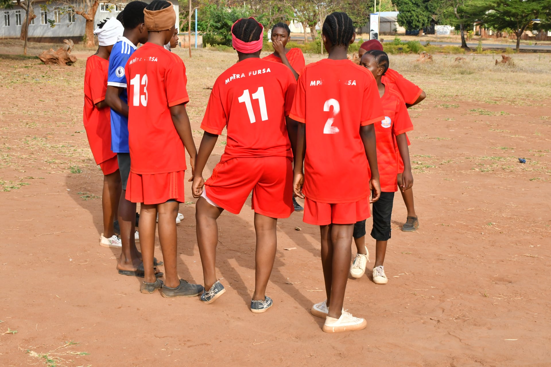 Mpira Fursa girls' team in red jerseys walking onto the pitch for a match