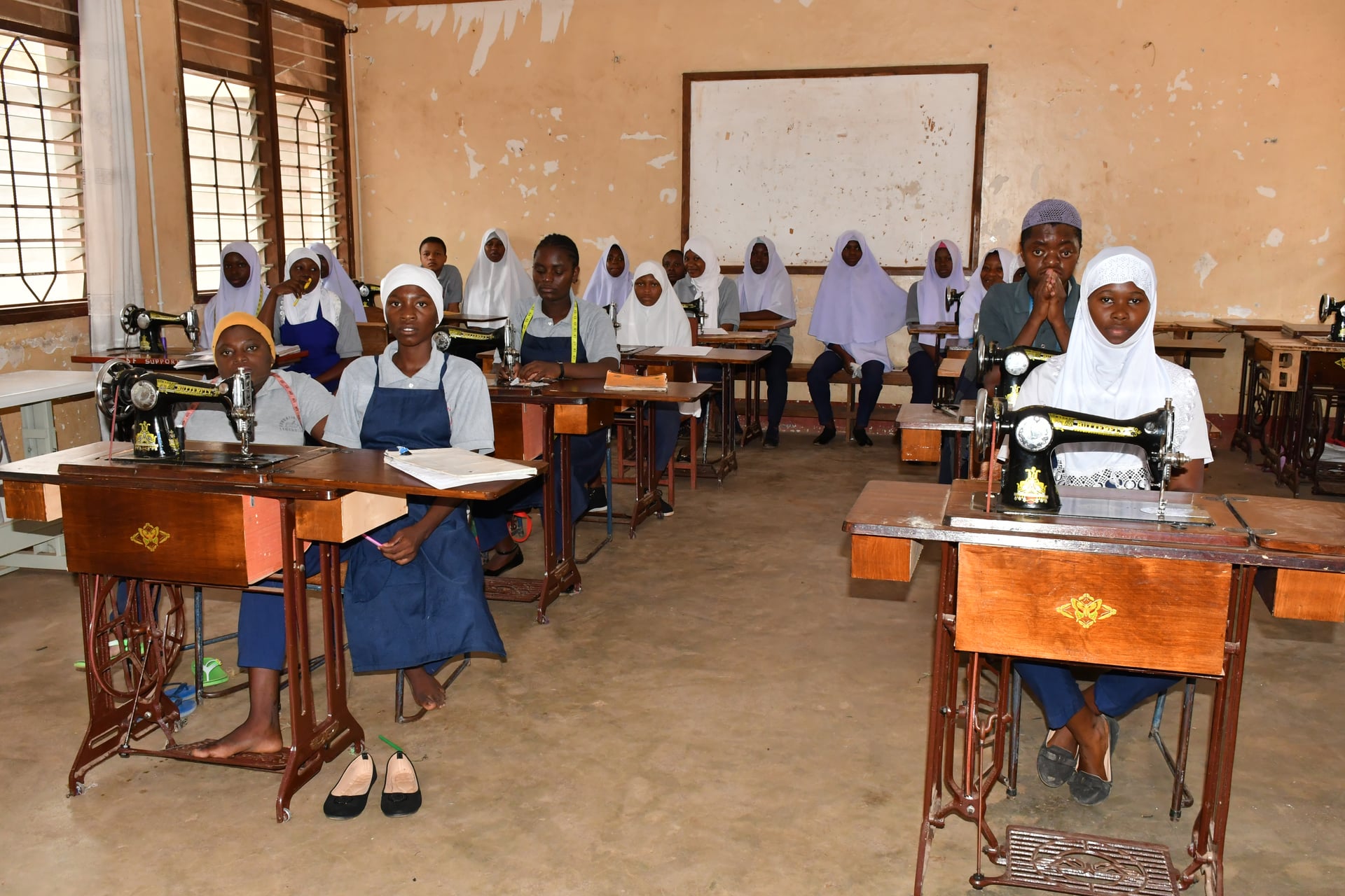 A full tailoring classroom of EHM students working together at rows of treadle sewing machines inside a Folk Development College